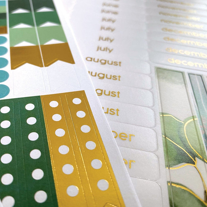 PL-2022E - Weekly Planner - Green Leaves - Close-up of open planner pages with green and gold decorative tabs, month labels, and white dot patterns on colored sections