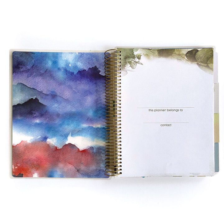 PL-2022E - Weekly Planner - Green Leaves - Spiral-bound planner open to ownership page with watercolor landscape cover featuring blue, purple, and red tones